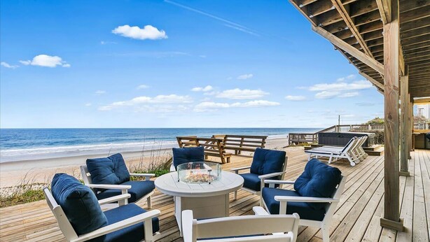 A wooden deck with outdoor seating, a glass-top table, and a view of the beach and ocean. - Once Upon a Tide Home with Hot Tub & Fire Pit (Ponte Vedra Beach)
