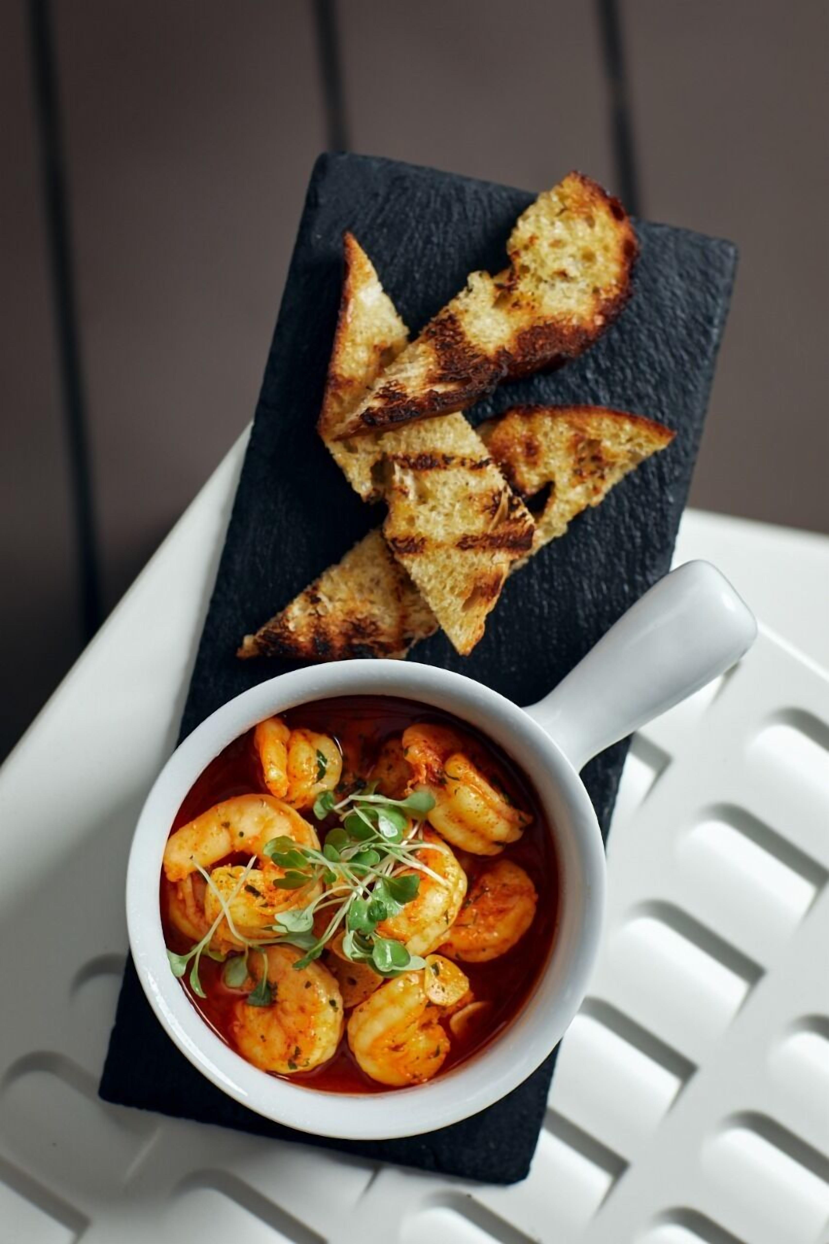 A bowl of shrimp pasta garnished with greens, accompanied by toasted bread on a slate board.