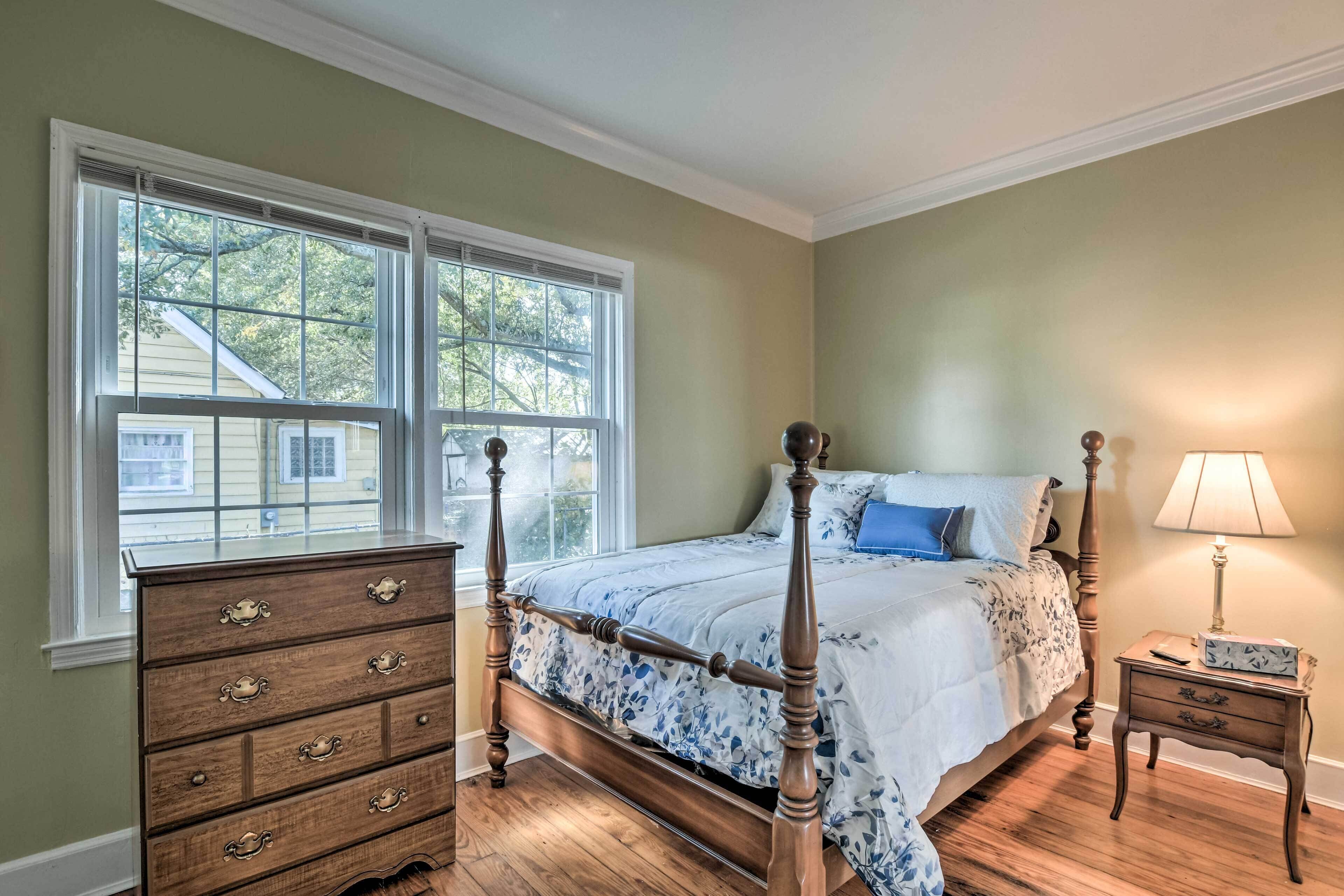 Une chambre à coucher avec un lit à baldaquin, une commode à tiroirs, une table de chevet avec une lampe et une fenêtre avec des stores.