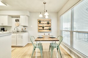 A modern kitchen with white cabinets, a wooden dining table, and a view through large windows.