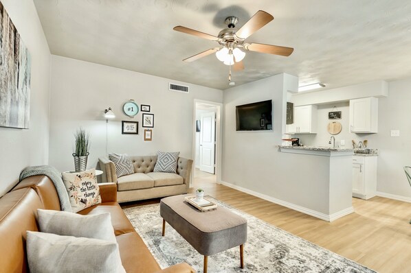A modern living room with a sofa, ottoman, and a ceiling fan.