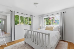 A bedroom with a white bed, a view of greenery outside, and a white door leading to another room. - Mid Century Modern-5 min from I-5 (Grants Pass)