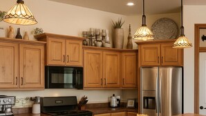 A modern kitchen with wooden cabinets, stainless steel appliances, and a central island with bar stools. - Hot Tub + 1,600 sq ft Golf-Course Patio • Game Room & Luxury Living (Billings)