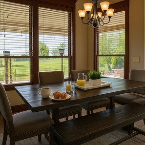 A dining area with a wooden table, chairs, and a bench. There is a pitcher of orange juice, a cup, and a plate with muffins. A potted plant is on the table. - Hot Tub + 1,600 sq ft Golf-Course Patio • Game Room & Luxury Living (Billings)