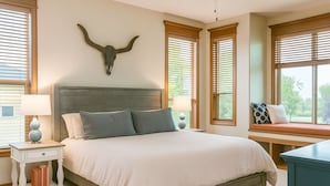 A bedroom with a large bed, two bedside tables, a ceiling fan, and a window seat with a view. - Hot Tub + 1,600 sq ft Golf-Course Patio • Game Room & Luxury Living (Billings)