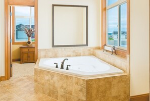 A bathroom with a freestanding bathtub, a wooden vanity, a large mirror, and a window with a view of houses. - Hot Tub + 1,600 sq ft Golf-Course Patio • Game Room & Luxury Living (Billings)
