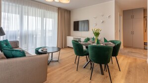 A modern living room with a dining area, a sofa with green cushions, a round table, and a flat-screen TV mounted on the wall. - Vacation apartment by the sea, vacation on the island of Usedom, Apartment SUN TOWERS B107 (Swinoujscie)