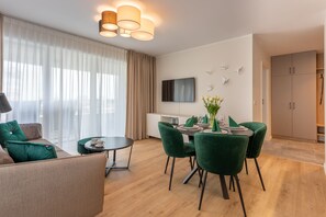 Ein modernes Wohnzimmer mit Essbereich, einer Couch mit grünen Kissen, einem runden Tisch und einem an der Wand befestigten Flachbildfernseher.