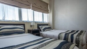 A hotel room with two beds, each with striped bedding, a bedside table with a lamp, and a window with a beige curtain. - Hotel Capelli Express (Talca)