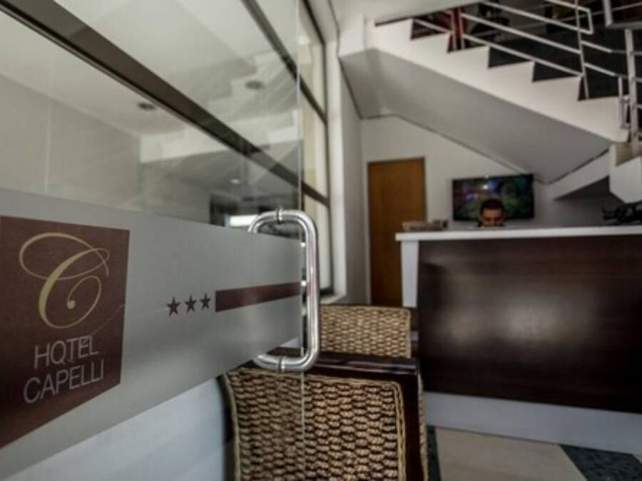 A modern hotel reception area with a glass partition displaying the logo and name "HOTEL CAPELLI".