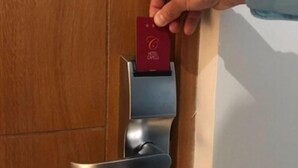 A hand inserting a red card into a modern, metallic door lock mechanism. - Hotel Capelli Express (Talca)