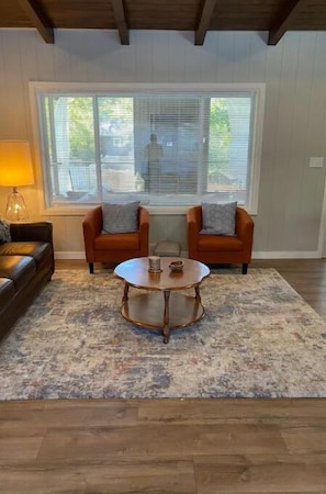 A living room with a sofa, two armchairs, a coffee table, and a window with blinds.