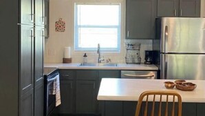 Une cuisine moderne avec des meubles de couleur sombre, un réfrigérateur en acier inoxydable et une chaise en bois.