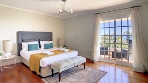 Une chambre à coucher avec un grand lit, des lampes de chevet, un banc, un tapis et une vue sur l’extérieur par une fenêtre.