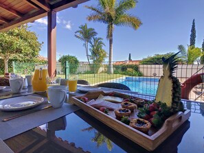 A breakfast table with a tray of pastries, a pitcher of orange juice, and a glass of water. - Ocean-View Villa ★ Private Pool and Garden (Caniço)