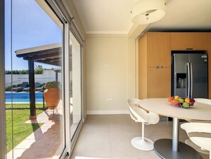 A modern kitchen with a built-in refrigerator, a dining area with a white table and chairs, and a large sliding glass door leading to a pool area. - Ocean-View Villa ★ Private Pool and Garden (Caniço)