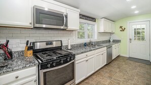 A kitchen with white cabinets, a stainless steel microwave, a gas stove, and a dishwasher. - Clean and Modern Home near Lk MI (Manistee)