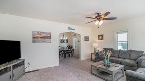 A living room with a television, a grey sofa, a coffee table, and a ceiling fan. - Clean and Modern Home near Lk MI (Manistee)