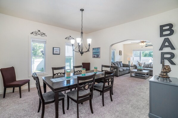 A dining area with a table, chairs, and a chandelier. There is a sofa and a coffee table in the background.