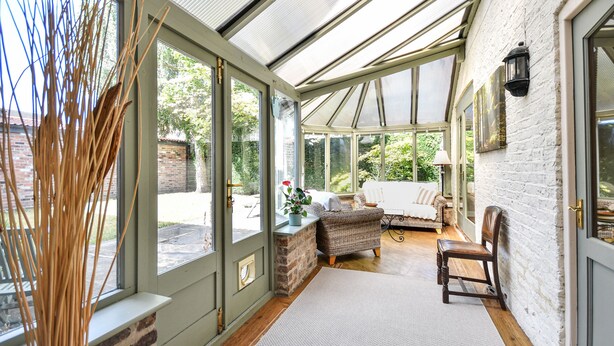 A conservatory with a brick wall, large windows, and a wooden floor. - Dovecote Farm House (Goole)