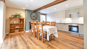 A dining area with a wooden table and chairs, a bookshelf, and a clock on the wall. - Dovecote Farm House (Goole)