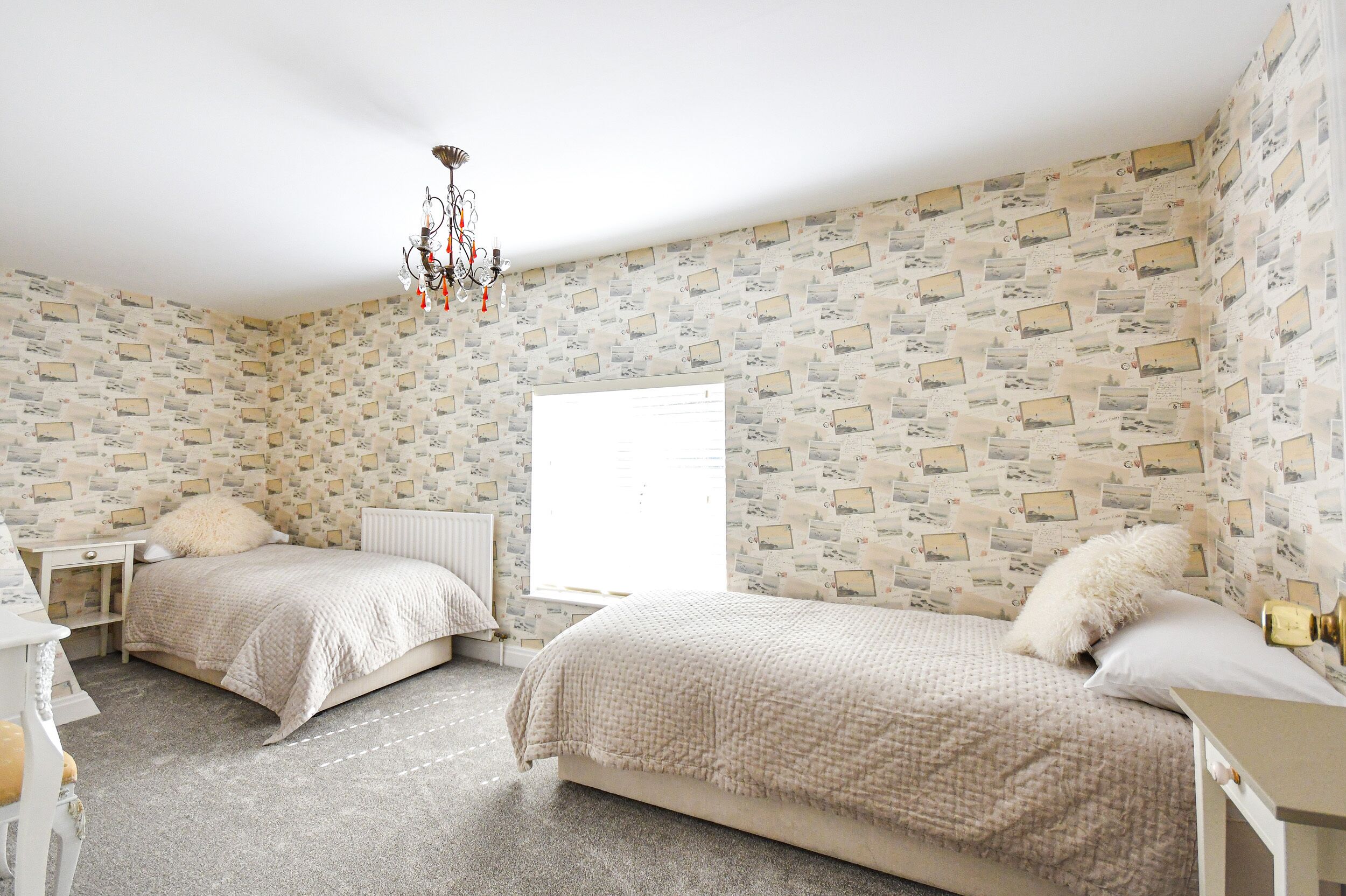 Une chambre avec deux lits, un radiateur blanc, un lustre et une fenêtre avec des stores.