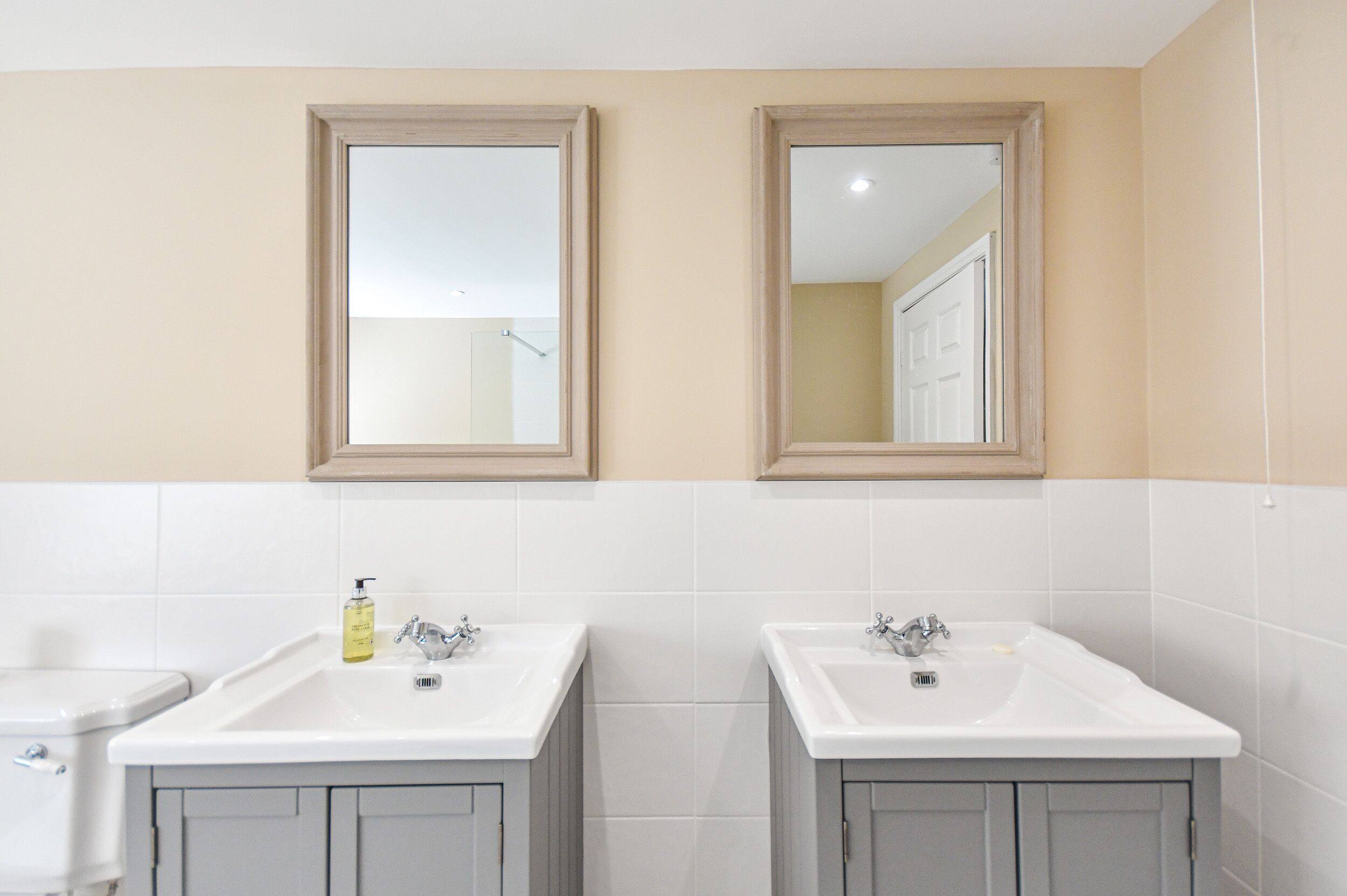 A bathroom with two sinks, a toilet, and a mirror above each sink.