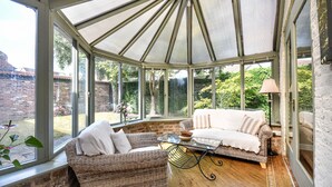 A conservatory with wicker furniture, a glass table, and a view of a brick wall and greenery outside. - Dovecote Farm House (Goole)