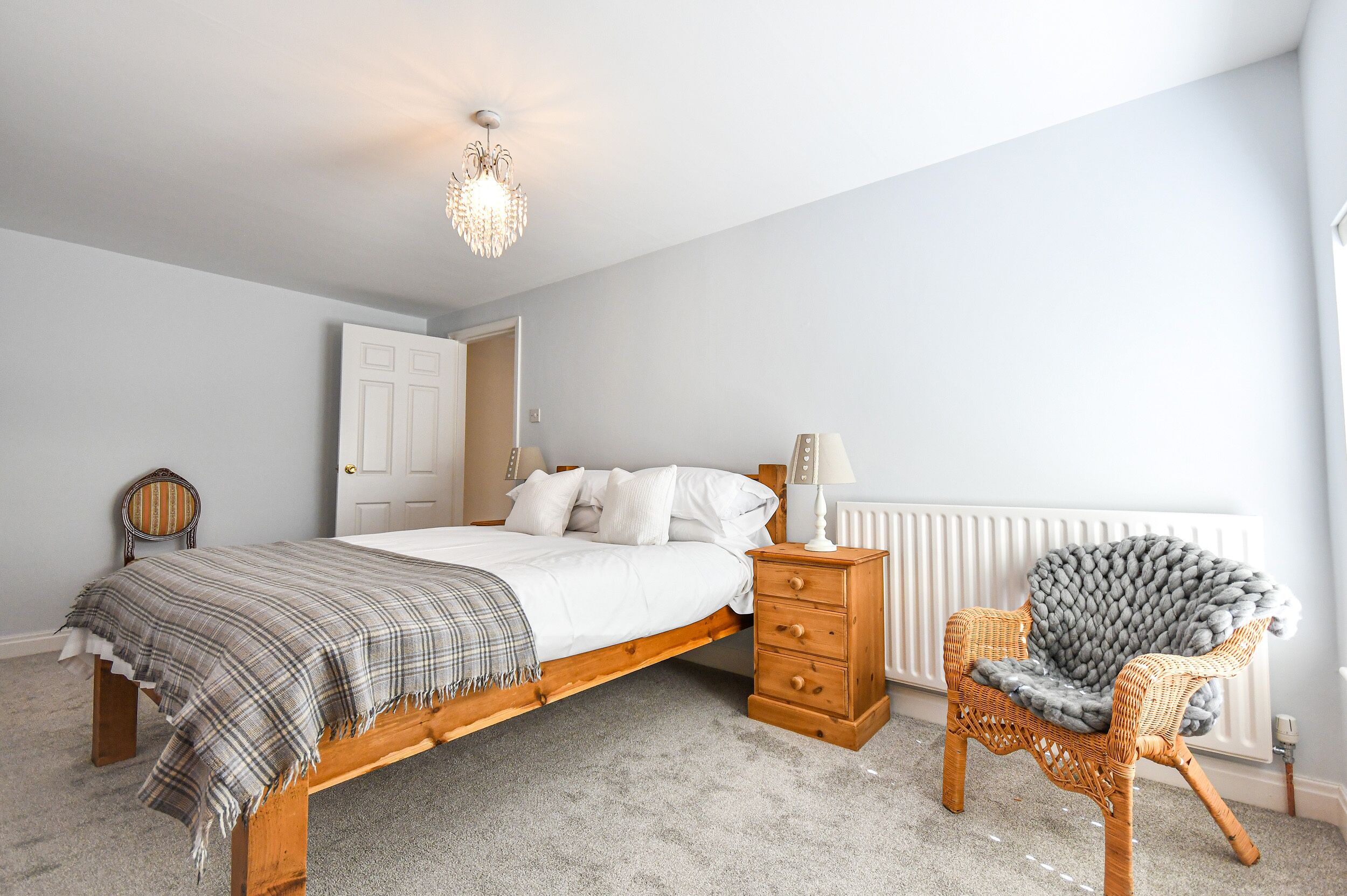 A bedroom with a wooden bed, a chair with a blanket, a dresser, and a chandelier.