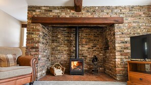 A cozy living room with a brick fireplace, a sofa, a TV stand, and a decorative statue. - Dovecote Farm House (Goole)
