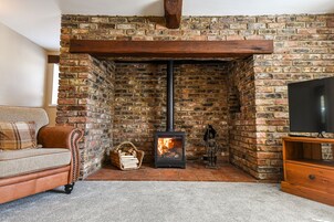 Una sala de estar acogedora con una chimenea de ladrillo, un sofá, un mueble para televisión y una estatua decorativa.