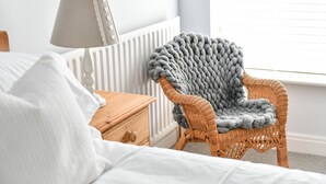 A bedroom with a bed, a nightstand, a wicker chair with a grey blanket, a lamp, and a radiator. - Dovecote Farm House (Goole)