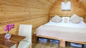 A cozy wooden room with a bed, a small table with a vase of flowers, and storage bins under the bed. - The Pod at Bank House Farm (Uttoxeter)