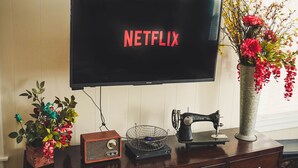 Een televisie met het Netflix logo, een vintage naaimachine en een bloemenvaas op een houten kast.