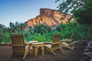 Une terrasse en bois, agrémentée de chaises Adirondack et d’une table, entourée de rochers et de verdure, avec une montagne en arrière-plan.