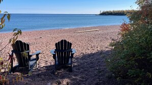 Ranta, jolla on kaksi Adirondack-tyylistä puutarhatuolia, jotka on asetettu vastakkain ja osoittavat merelle. Tuoleja ympäröivät puut ja pienet kivet.
