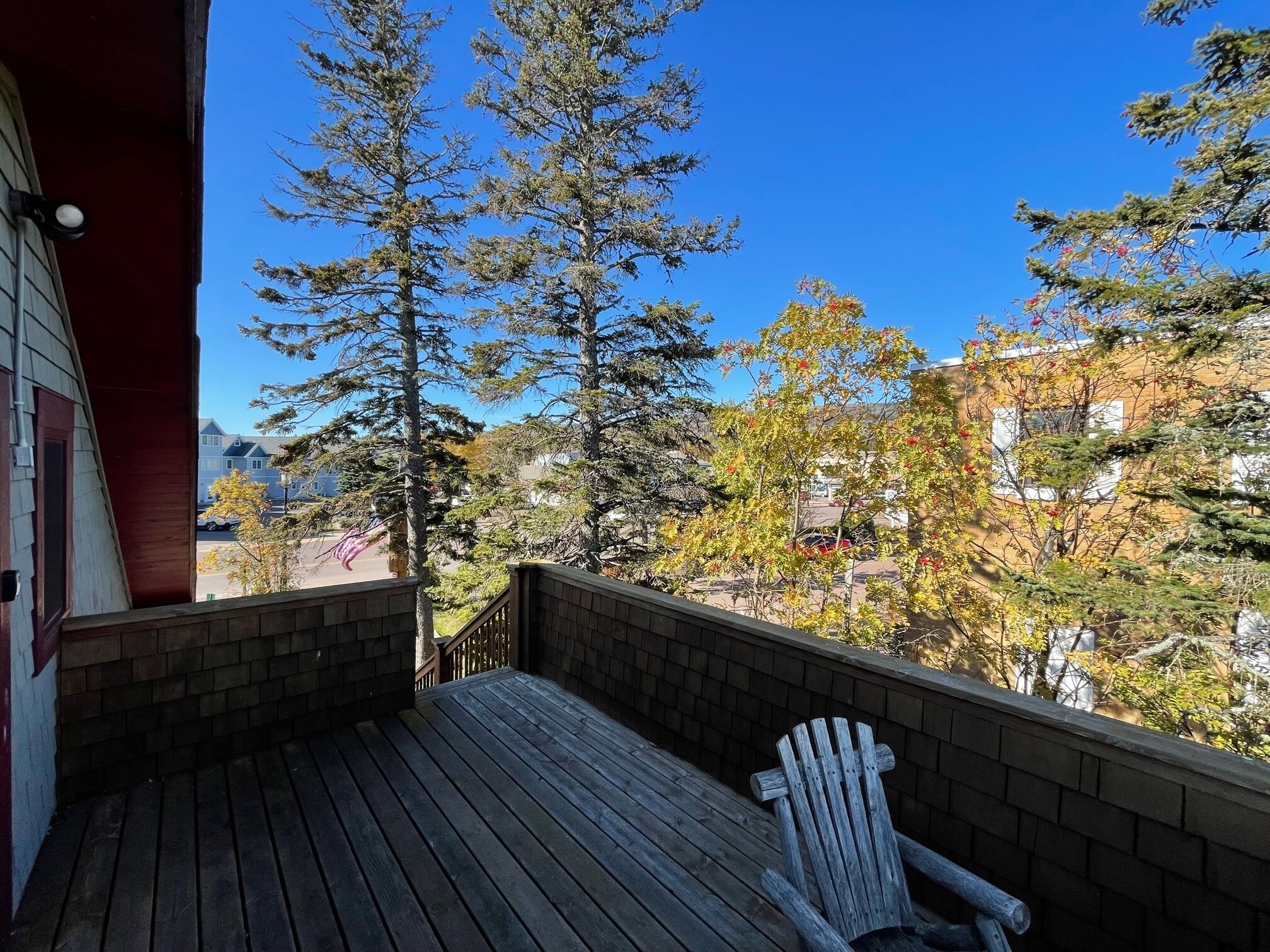 A wooden deck with a chair, overlooking a residential area with trees and houses.