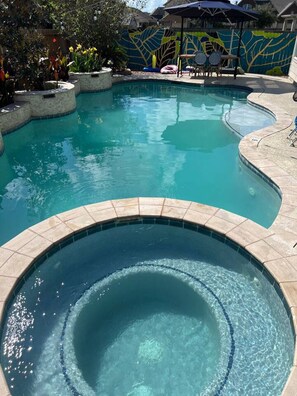 A swimming pool with a hot tub in the foreground, surrounded by a decorative wall and outdoor seating.