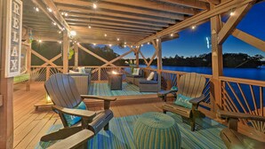 Een terras buiten met houten meubilair, lichtjes en uitzicht op het water.