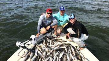 Trois personnes se trouvent dans un bateau, entourées d’une grande quantité de poissons.