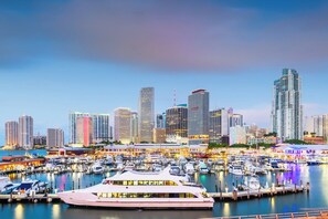 Un port de plaisance où sont amarrés de nombreux bateaux, un restaurant situé au bord de l’eau et une vue sur les toits de la ville, avec ses nombreux immeubles de grande hauteur.