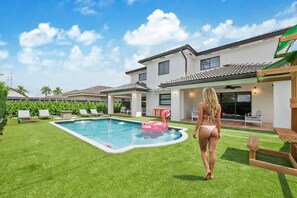 A residential backyard with a swimming pool, a pink flamingo float, and a house with a patio.