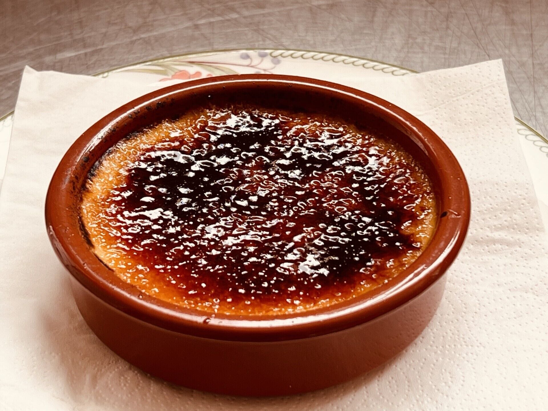 A ramekin with a dessert, possibly crème brûlée, on a napkin.