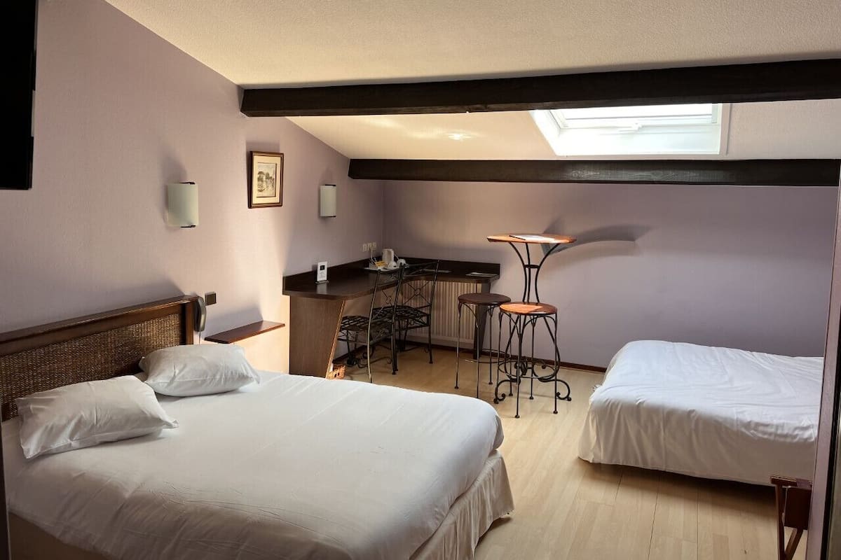 Une chambre d’hôtel avec deux lits, une kitchenette, un petit coin repas et une lucarne.