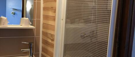 A bathroom with a wooden wall, a sink with a mirror, and a shower with a textured glass door.