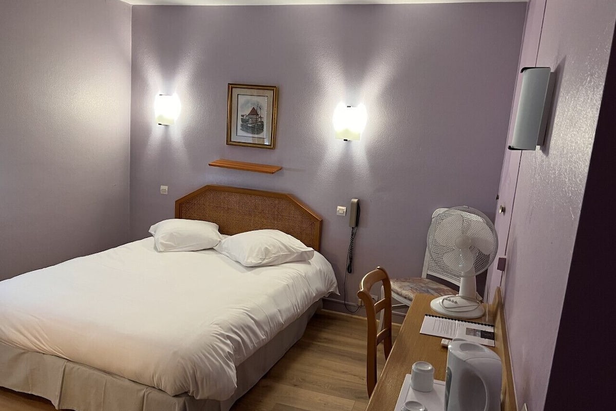 Une chambre à coucher avec un lit, une table de chevet, une chaise et un ventilateur.