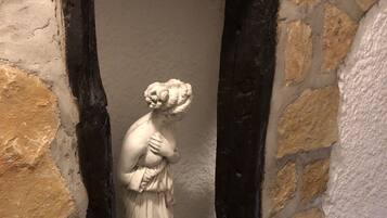 Una estàtua de marbre d'una dona ubicada en una m niche amb un mur de pedra al fons.