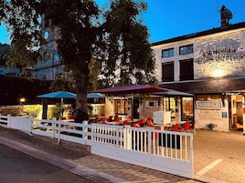 Un restaurante con terraza, una cerca blanca y un edificio con una torre de reloj al fondo.