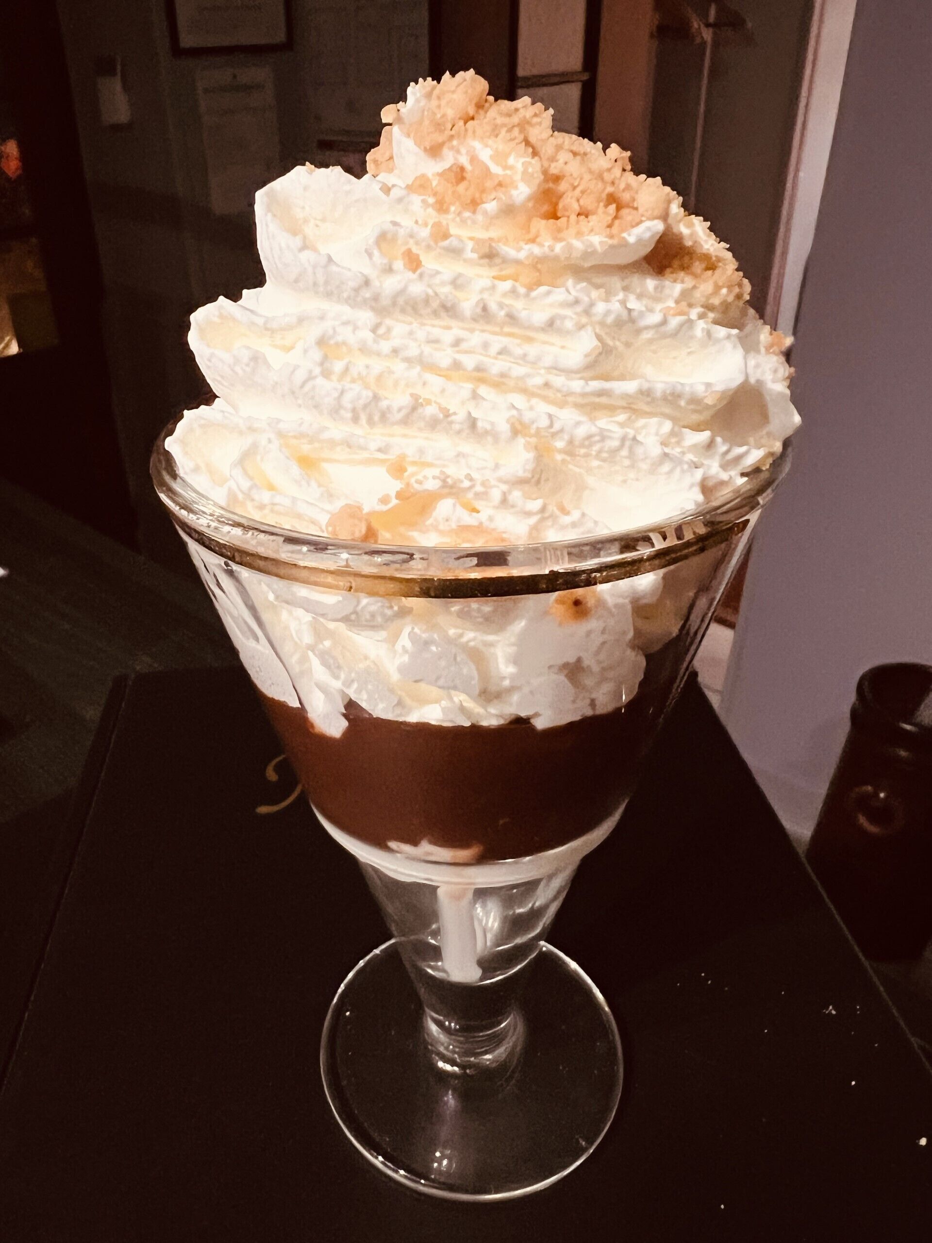 A dessert in a glass bowl with whipped cream and caramel on top.