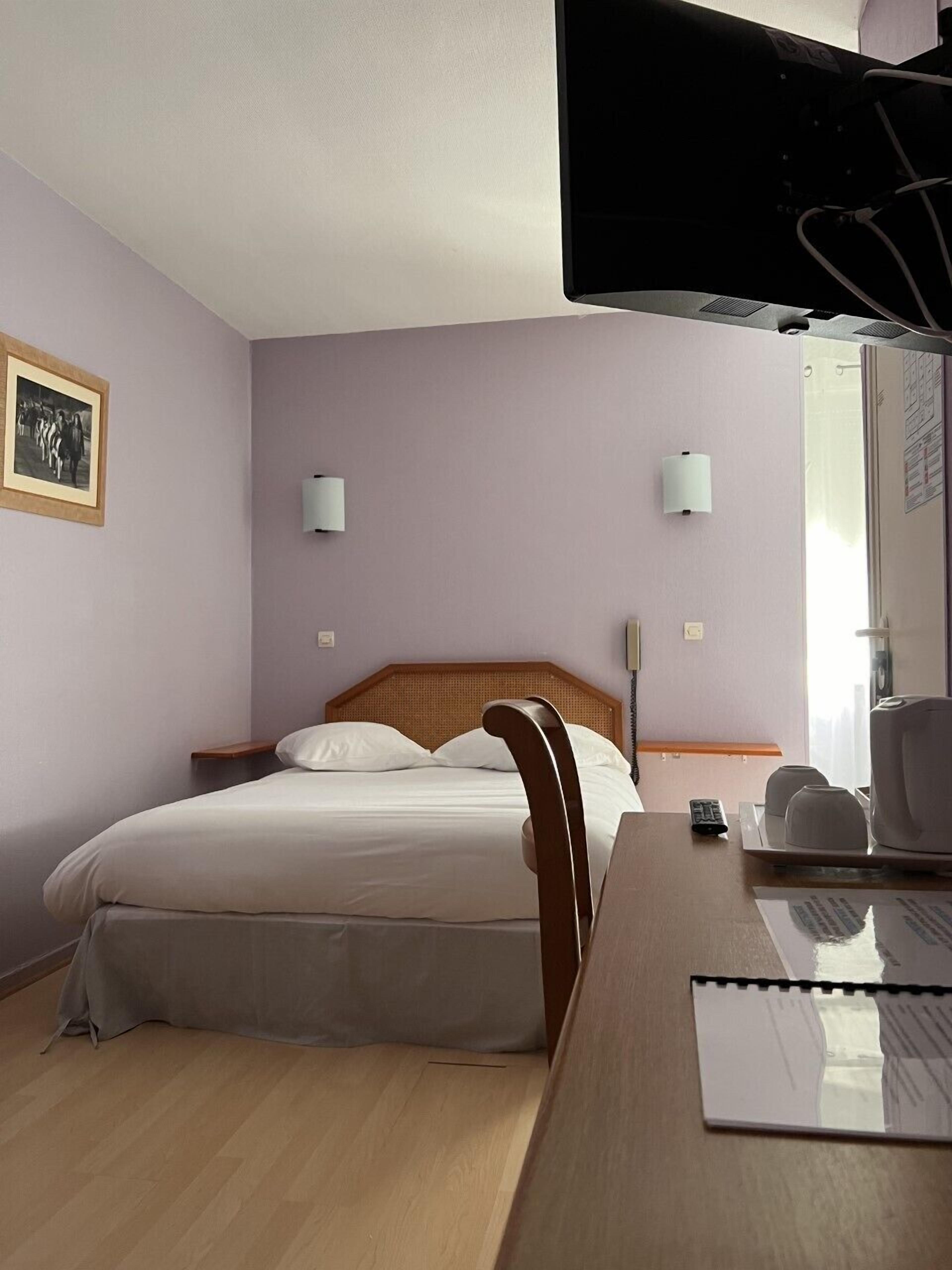 A hotel room with a bed, a desk, a chair, a television, and a window.